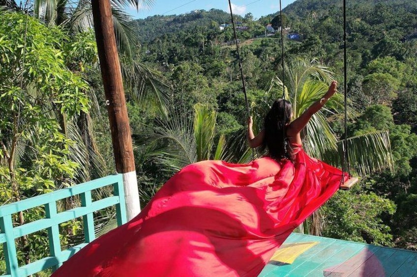 A person in a red dress swinging on a swing with a lush green landscape in the background. 3