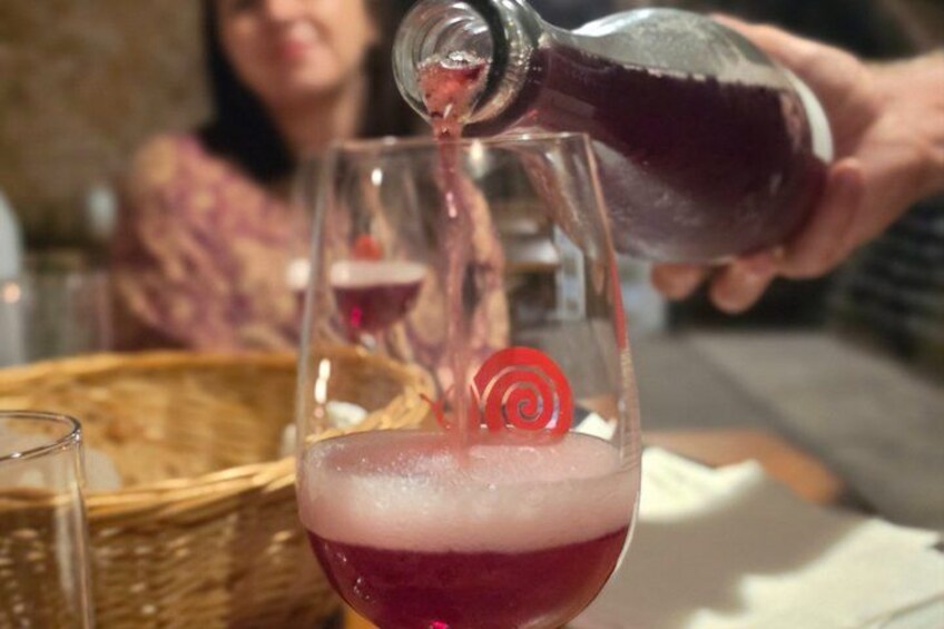 A person pouring a dark liquid into a glass with a red swirl garnish. 4