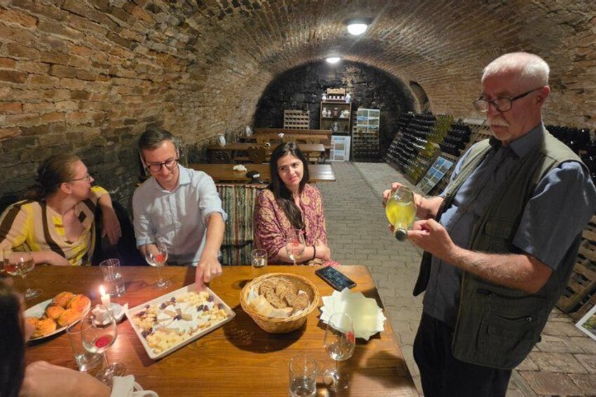 A group of people dining in a cellar with wine bottles and a wooden table. 2