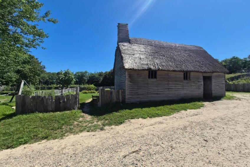 A thatched-roof wooden house with a dirt path leading to it, surrounded by greenery and a clear sky. 5