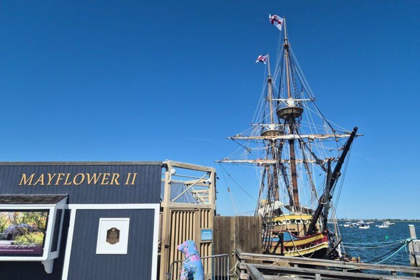 A tall ship docked at a pier with a sign reading 'MAYFLOWER II'. 1