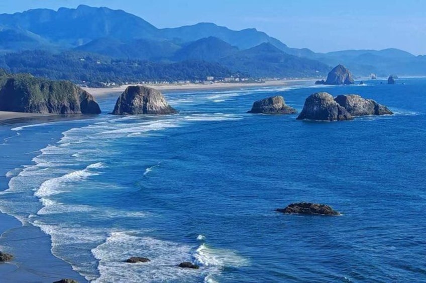 A coastal landscape with a sandy beach, ocean waves, and large rock formations. 5