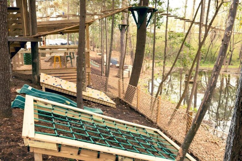 A playground with wooden climbing structures and a rope bridge over a body of water. 5