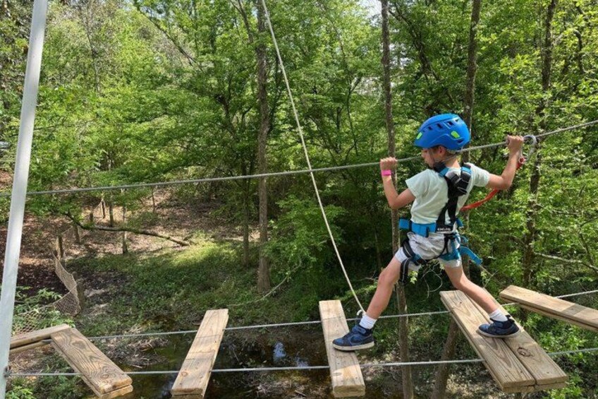 A person navigating a rope bridge in a forested area. 4