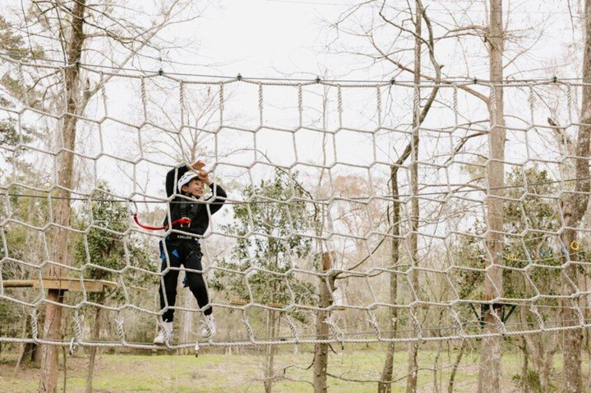 A person navigating a rope bridge in a wooded area. 1