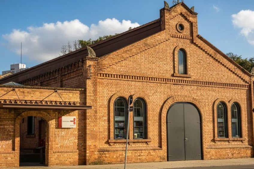 A brick building with a large arched entrance, a small tower, and a signboard. 5