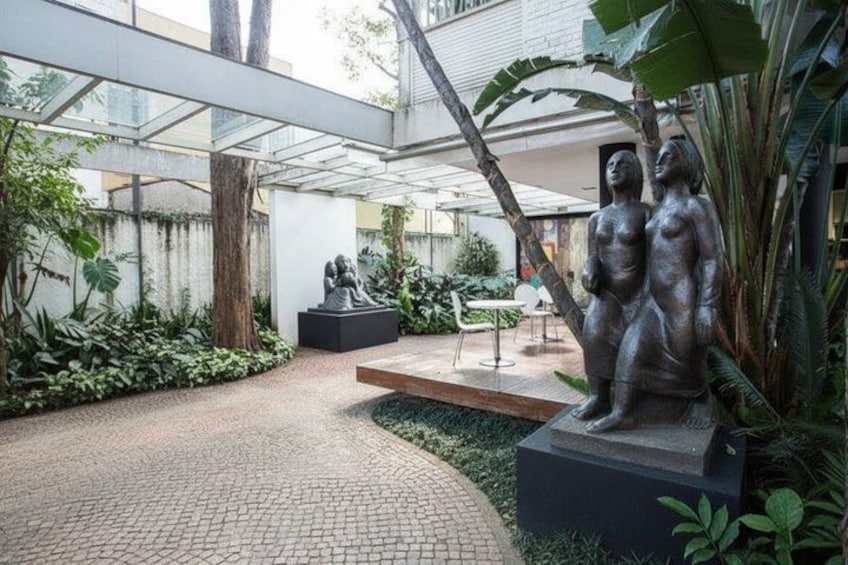 A courtyard with a statue, a bench, and lush greenery. 1
