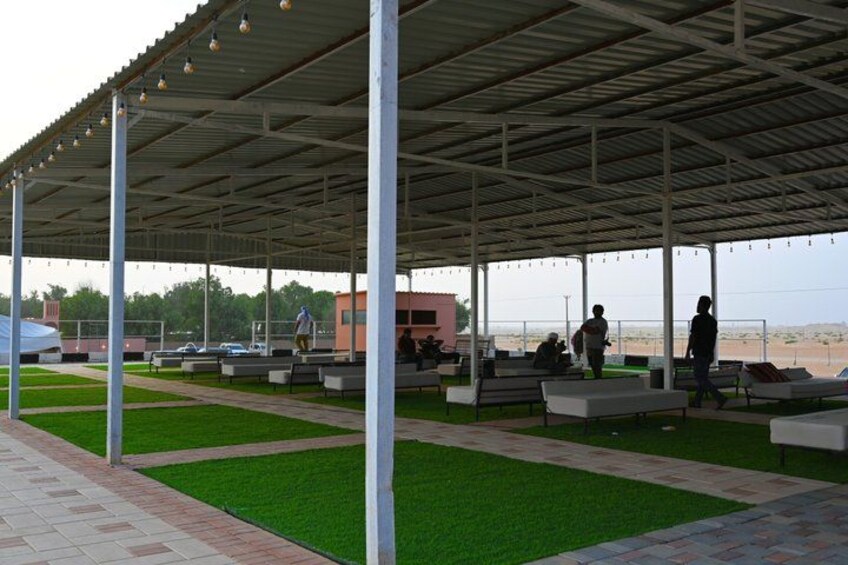 A covered outdoor seating area with benches and artificial grass, overlooking a beach. 5