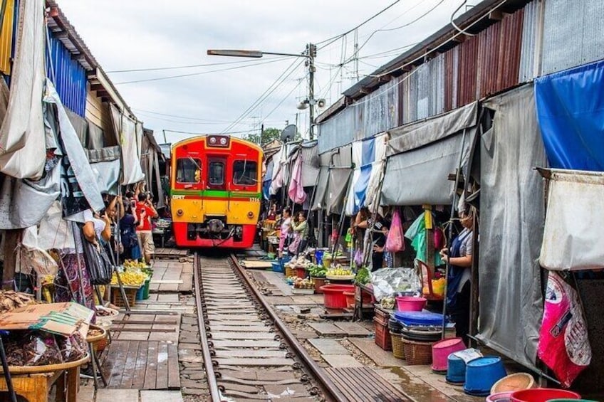 A train on tracks in a market area with stalls and people. 1