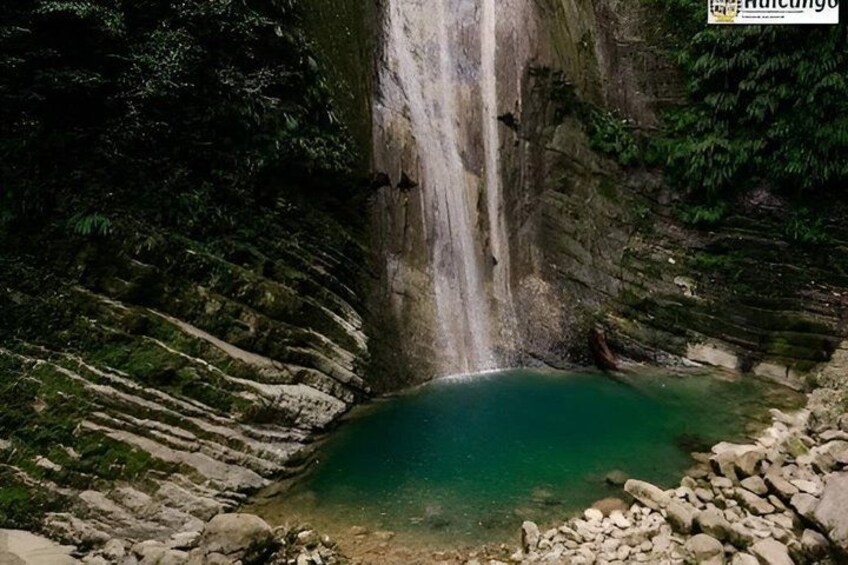 A waterfall cascading into a turquoise pool surrounded by rocky terrain and dense forest. 3