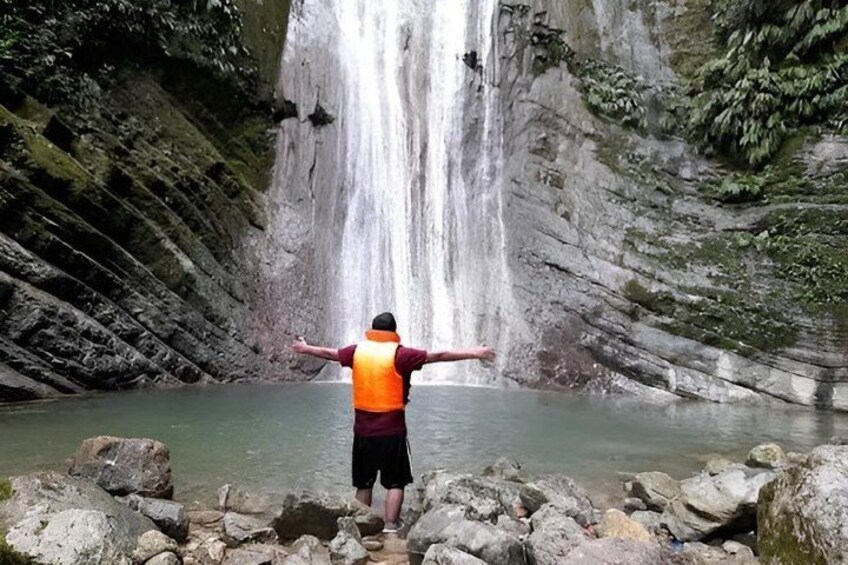 A person in a life jacket standing on rocks by a waterfall. 2