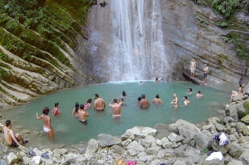 A group of people in a natural hot spring surrounded by rocks and greenery. 4