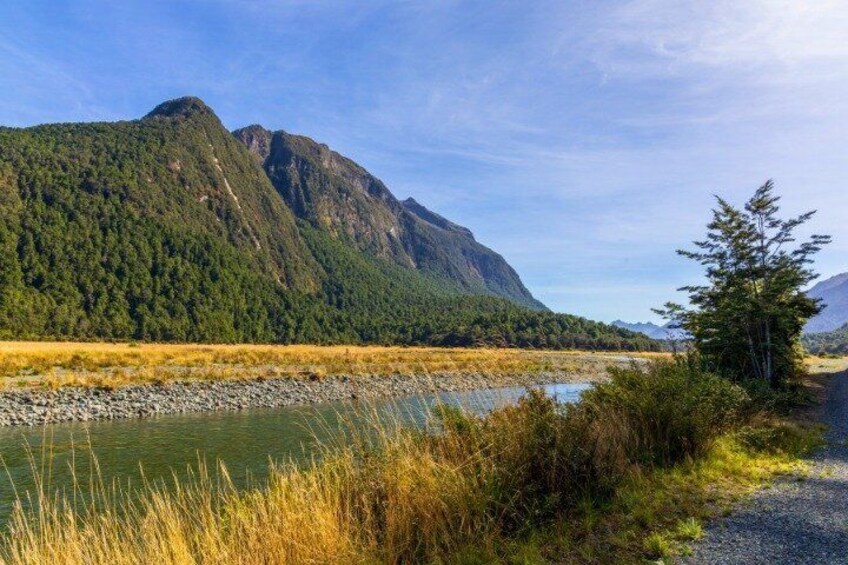 A river, grassy banks, a mountain, and a clear sky. 5