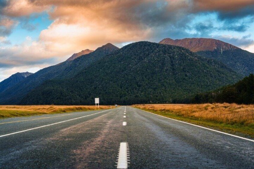 A road leading towards a mountain range with a cloudy sky. 1