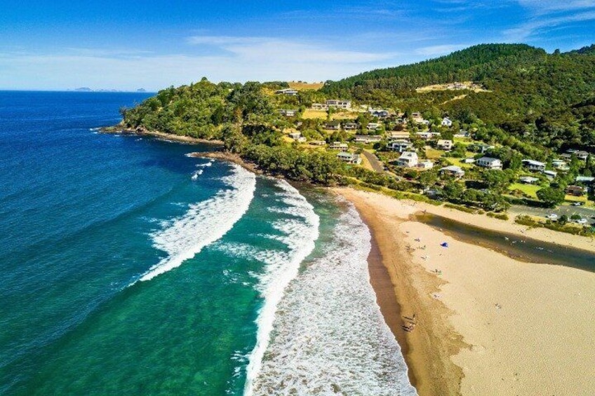 A coastal landscape with a beach, ocean waves, and a hillside with houses. 4