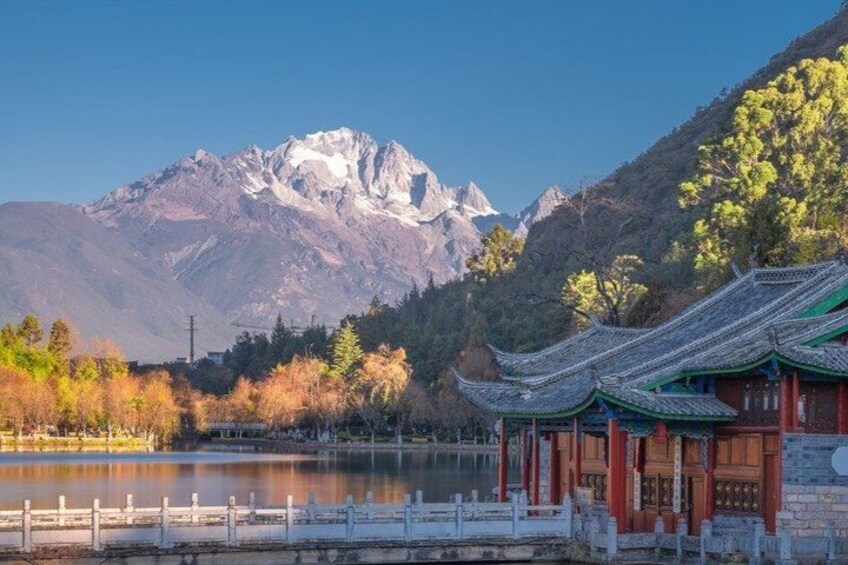 A traditional building with a tiled roof, a body of water, and mountains in the background. 2