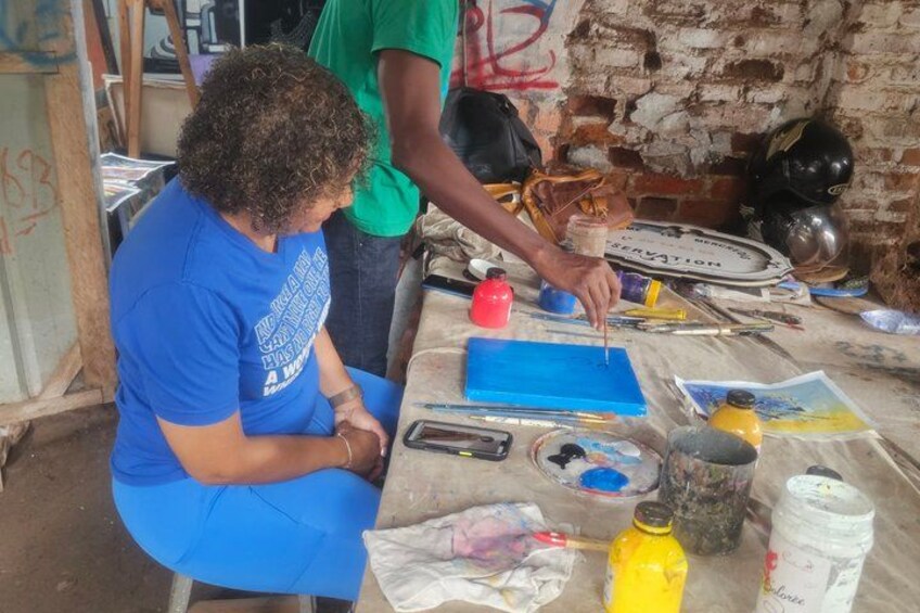 A person painting on a canvas with various art supplies on a table. 4