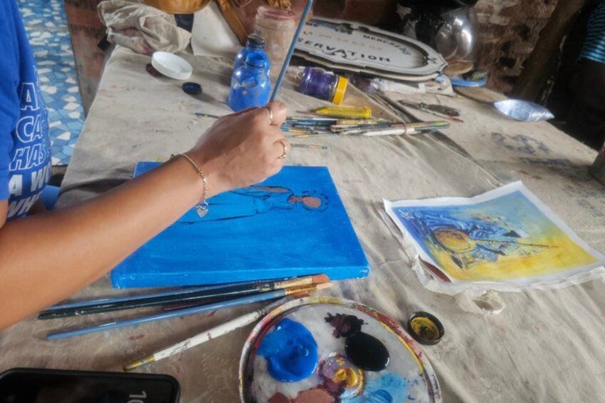 A person painting on a blue canvas with various art supplies scattered around. 3