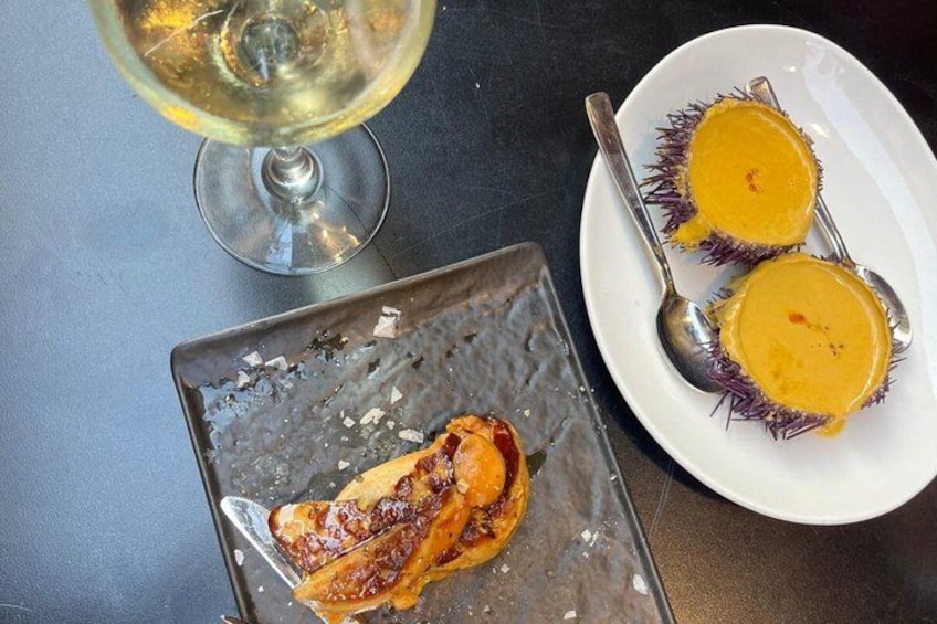 A plate with two yellow desserts, a glass of white wine, and a metal tray with a dessert. 5