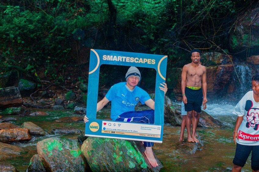 A person holding a framed photo with the text 'SMARTESCAPES' in a natural setting with rocks and a waterfall. 3