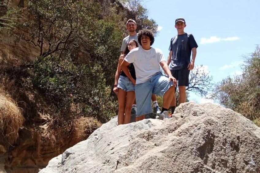 A group of people standing on a rocky outcrop with sparse vegetation and a clear sky. 4