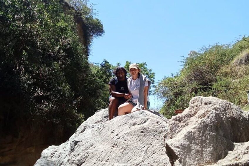 Two people sitting on a rocky outcrop with a canyon and greenery in the background. 5