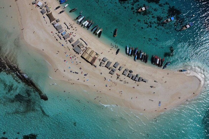 A beach with sun loungers, a small structure, and boats in the water. 4