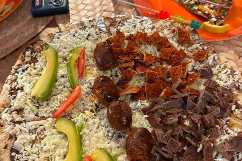 A pizza with toppings like avocado, red peppers, and meat. 5