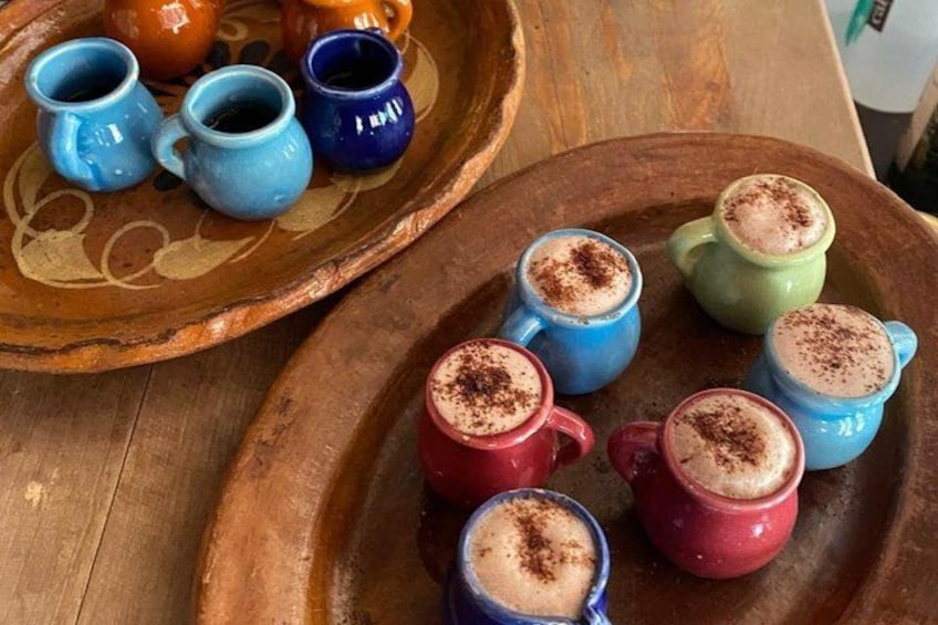 A wooden tray with colorful ceramic mugs filled with a frothy beverage, some with a sprinkle of a brown powder on top. 1