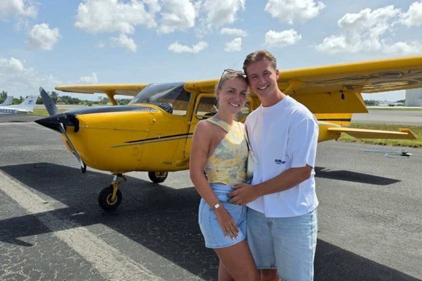 A small yellow aircraft on a tarmac with a person standing in front of it. 2
