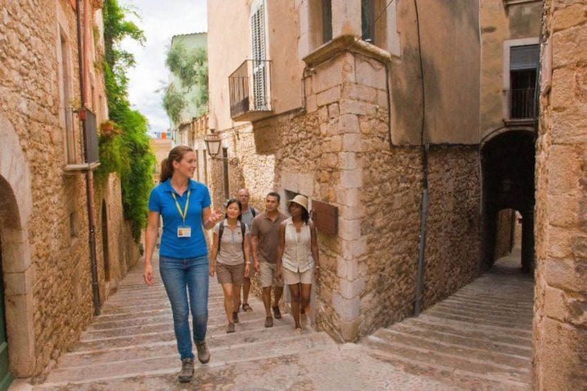 A narrow stone pathway flanked by buildings, a person leading a group, and a horse. 4
