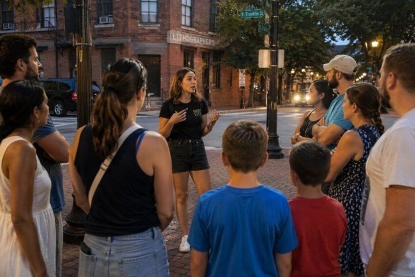 A group of people standing on a sidewalk, facing a street corner. 1