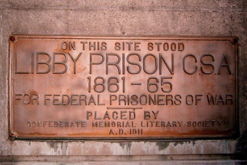 A weathered metal plaque on a wall, commemorating Libby Prison CSA, operational from 1861 to 1865, for federal prisoners of war, placed by the Confederate Memorial Literary Society in 1911. 2