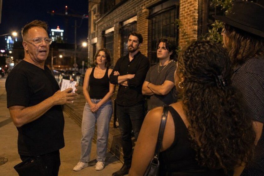 A group of people standing on a sidewalk at night, engaged in conversation. 5