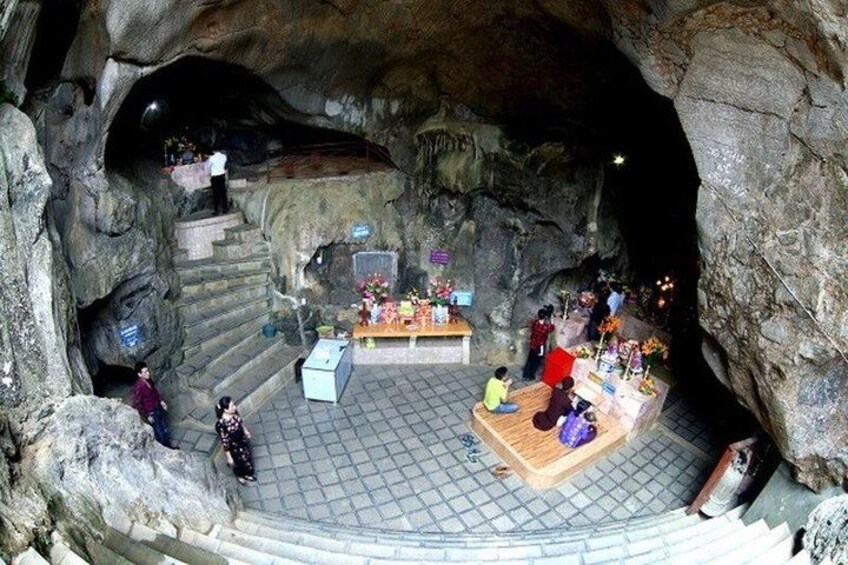A cave with a central altar, stone steps, and visitors. 2