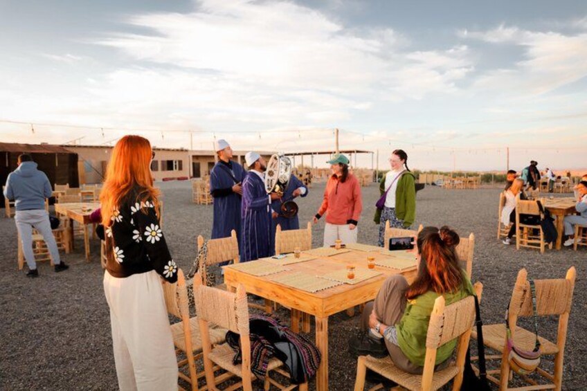 A group of people gathered around a wooden table outdoors, possibly at a social event or meeting. 4