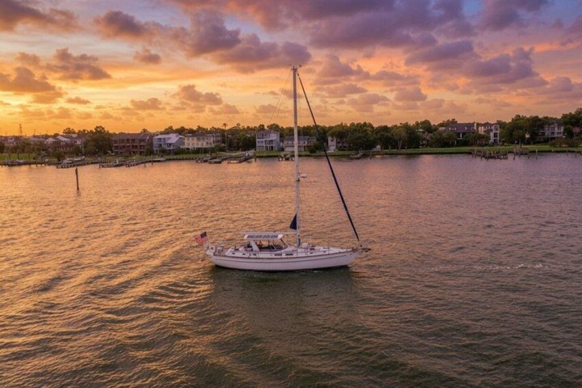 A sailboat on calm water during sunset with a residential area in the background. 1
