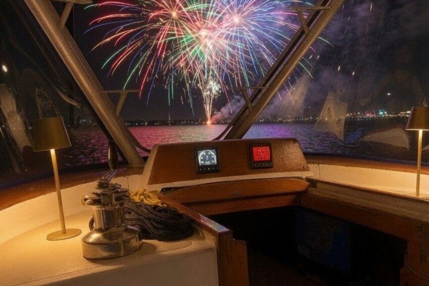 A boat's control panel with a digital display and a view of fireworks over water. 3