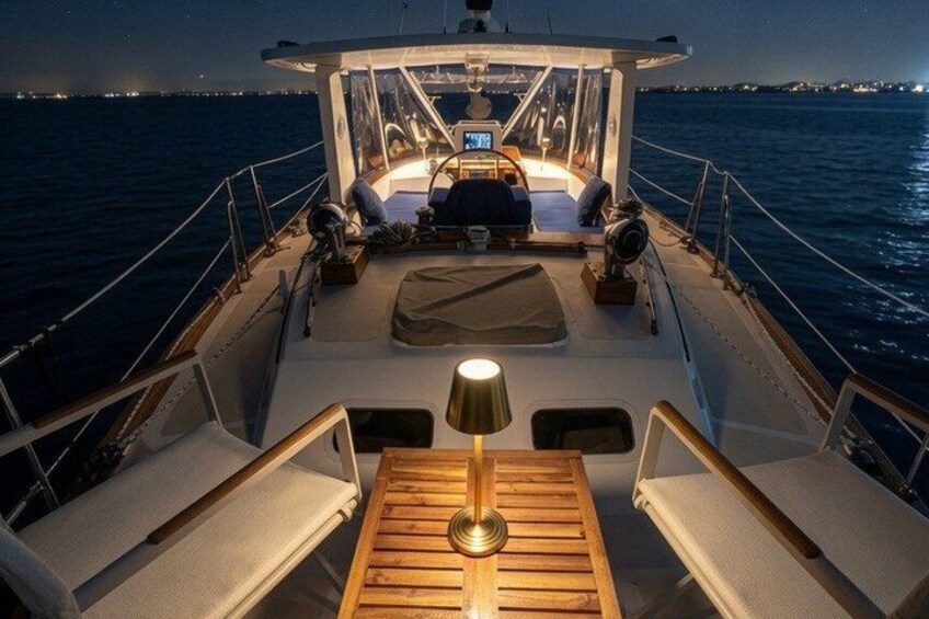 A boat deck at night with a table, chairs, and a steering wheel. 2
