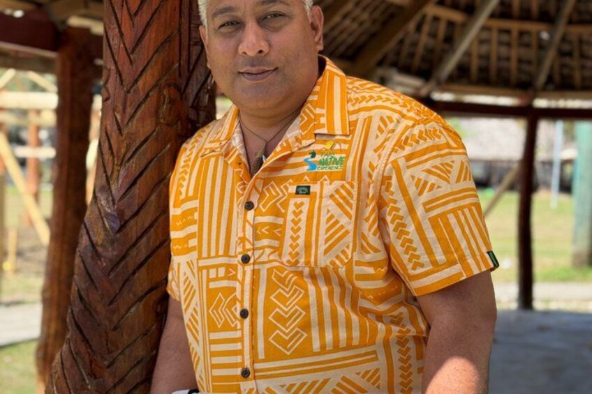 A person wearing a patterned shirt with a logo, standing next to a wooden structure with a carved design. 3