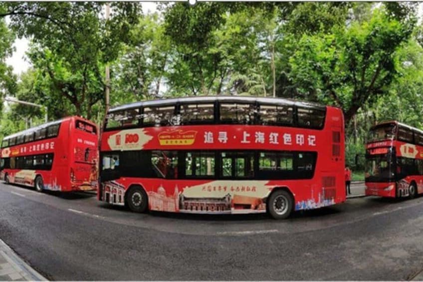 A red double-decker bus with advertisements on its side, parked on a street with trees in the background. 2