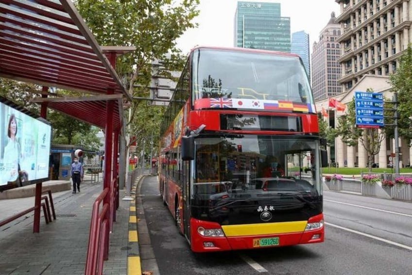 A double-decker bus at a bus stop with a cityscape in the background. 3