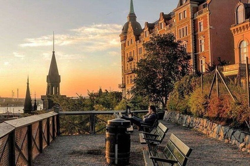 A riverside walkway with benches, a large building with a tower, and a church spire in the background. 1