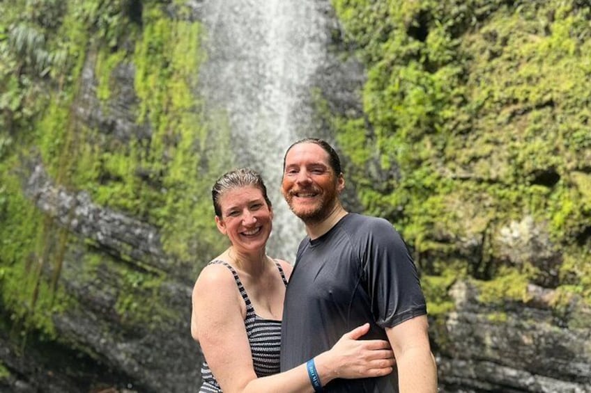 A couple standing in front of a waterfall with moss-covered rocks. 3