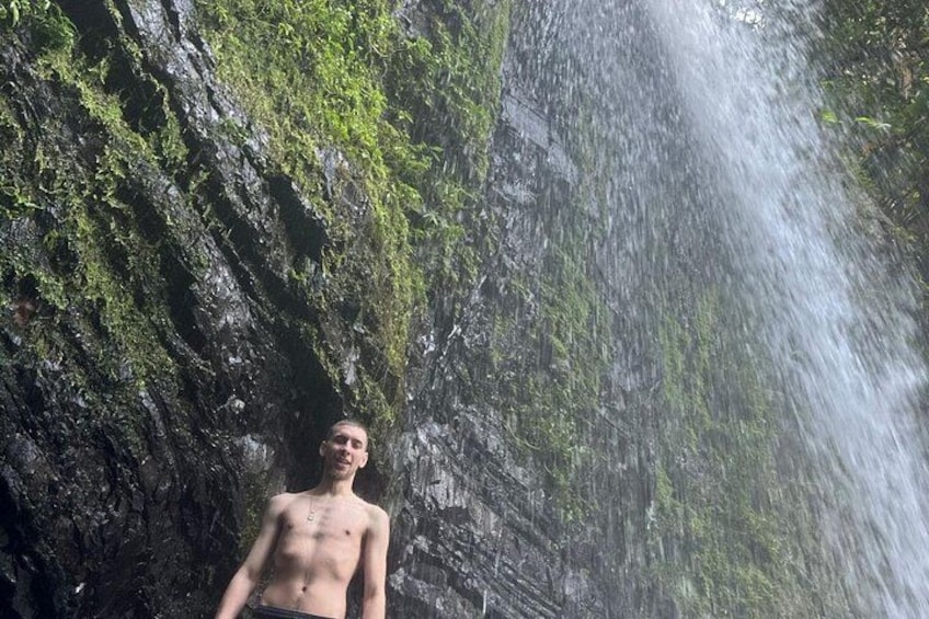 A person standing in front of a waterfall with a rocky cliff and greenery. 4