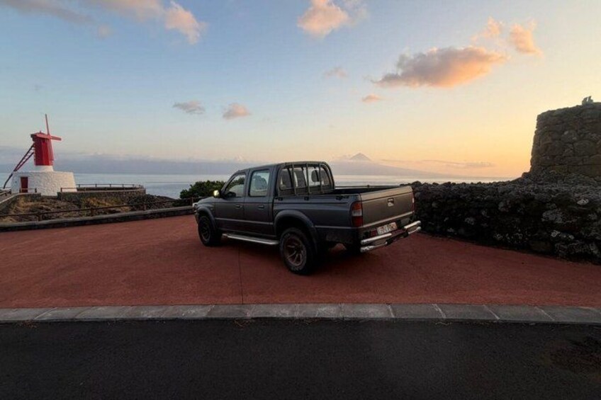 A pickup truck parked on a red surface near a lighthouse and a stone wall. 5