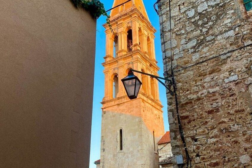 A tall tower with a clock, a street lamp, and a stone wall. 2