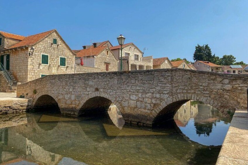 A stone bridge over a calm water body, with buildings and a clear sky in the background. 3