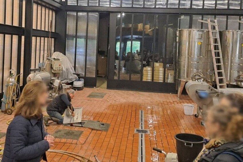 A brewery interior with brewing equipment, a brick floor, and a large door leading outside. 2