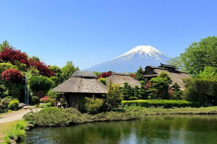 A traditional Japanese garden with a pond, thatched-roof structures, and Mount Fuji in the background. 2